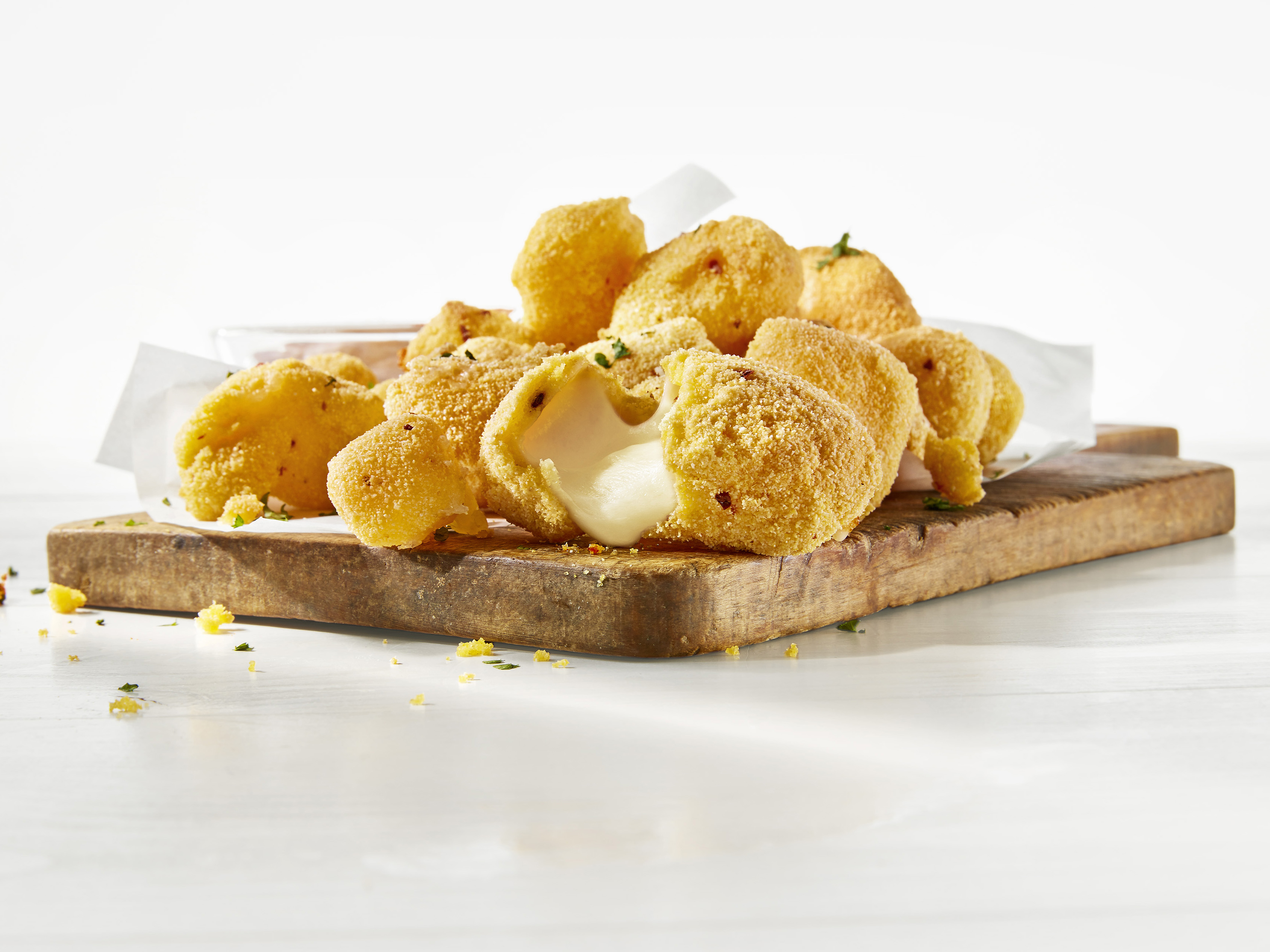 Frittierte Cheese Curds auf einem Holzbrett. Aus einem Bällchen fließt Käse heraus. Frittierte Cheese Curds auf einem Holzbrett. Aus einem Bällchen fließt Käse heraus.
