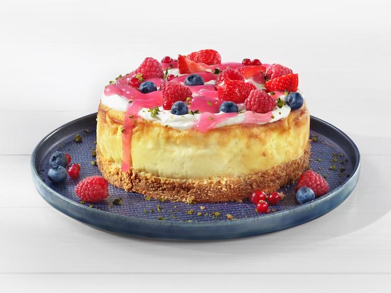 Cheesecake mit einem Topping aus MILRAM Schmand, roter Grütze und frischen Beeren auf einem blauen Teller