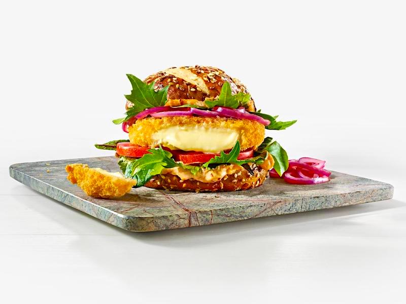 Burger mit paniertem Cheese-Patty, Rucola, Tomatenscheiben, Zwiebelscheiben und Kimchi-Mayonnaise 