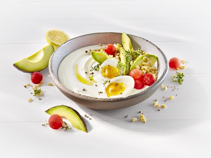 MILRAM Joghurt Griechischer Art in einer Schale garniert mit zwei halben gekochten Eiern, Avocado-Stückchen, Wassermelone-Kugeln und Sonnenweizen