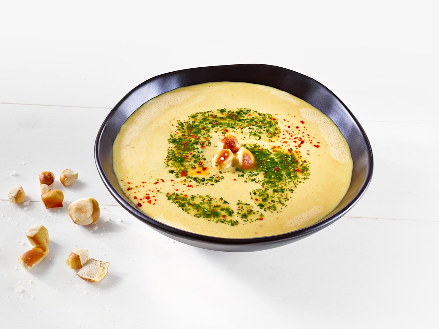 Suppe mit MILRAM Gouda-Alternative serviert in einer Schale, garniert mit Kräutersauce und Brezel-Croûtons