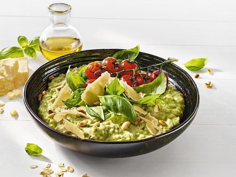 MILRAM Porridge verfeinert mit Basilikum-Pesto, in einer schwarzen Schale, getoppt mit Ofentomaten, Pinienkernen und Parmesanraspeln