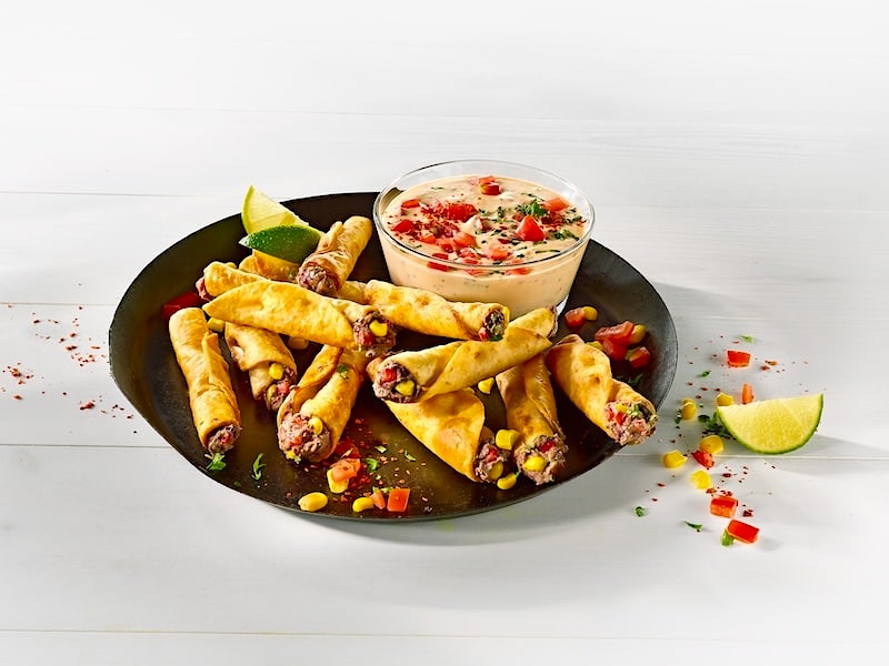 Runder Teller mit Taquitos gefüllt mit Hackfleisch, Mais und roter Paprika; daneben ein Schälchen mit Käsedip