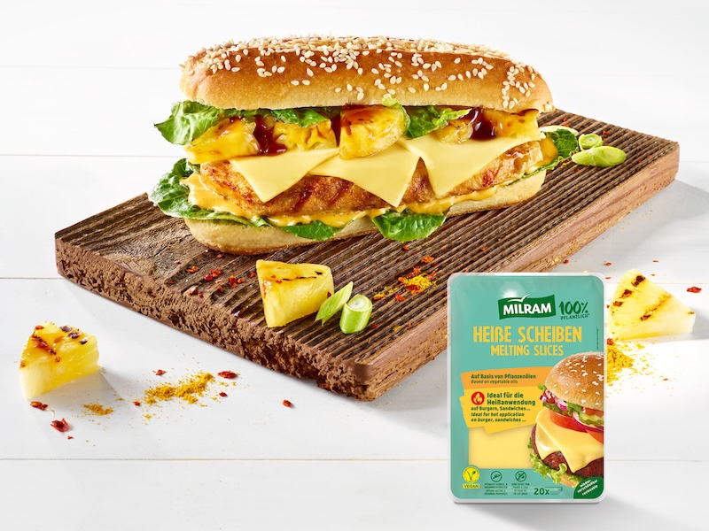 No-Chicken-Sandwich auf einem Holzbrett; belegt mit Salat, veganem Hühnchen-Fleisch, MILRAM Heiße Scheiben und gegrillten Ananas-Stückchen