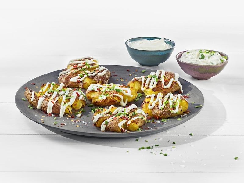 Smashed Potatoes auf einem runden Teller; getoppt mit Limetten-Dip aus MILRAM Schmand sowie Chili-Flocken und gehackter Petersilie
