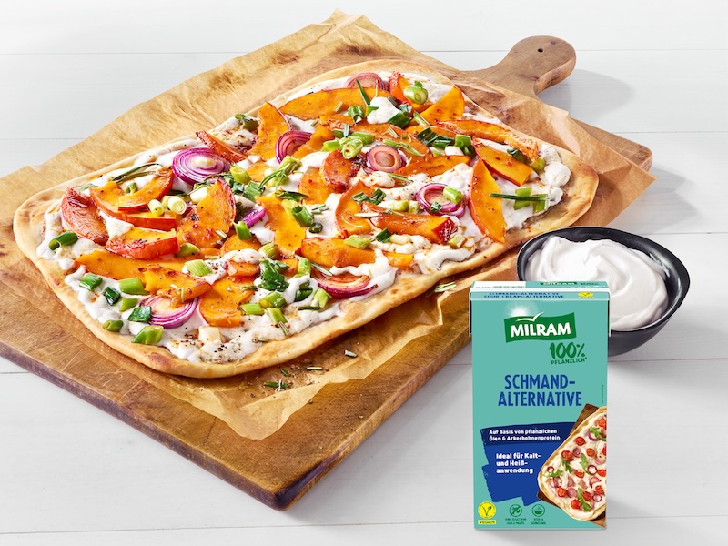 Rechteckiger Flammkuchen auf einem Holzbrett belegt mit MILRAM Schmand-Alternative