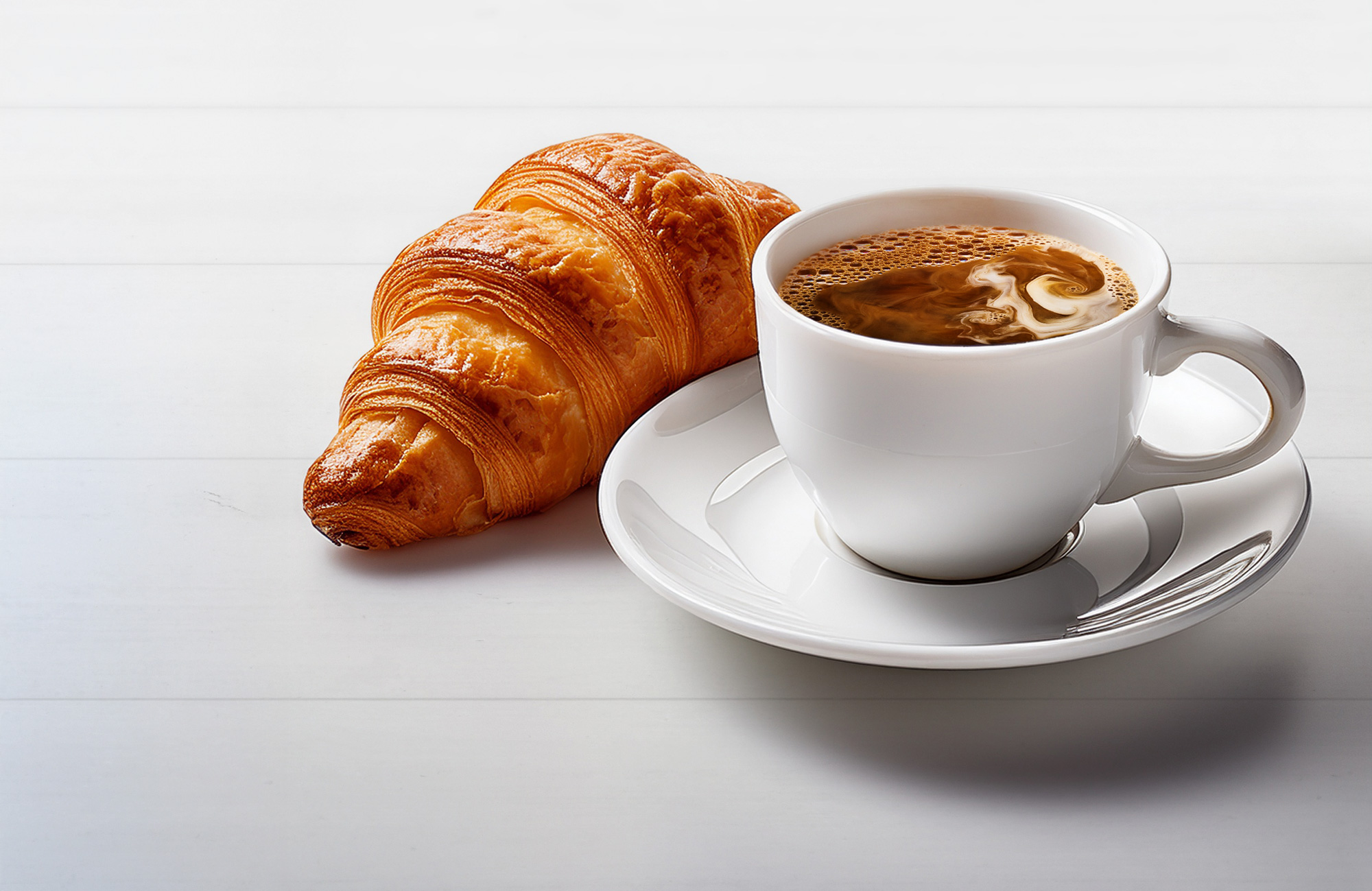Ein Kroasan und eine Tasse Kaffee auf einem Tisch