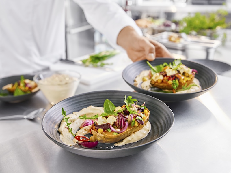 Zwei Teller mit MILRAM PaprikaQuark und einer Süßkartoffel-Kumpir, getoppt mit roter Zwiebel, Mais, Feta und Rucola