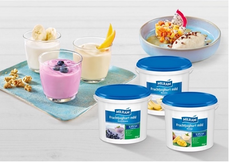 Im Hintergrund ein Teller mit Frozen-Bananen-Joghurt und Obstsalat; davor Mango-, Heidelbeer- und Bananenjoghurt angerichtet in drei Gläschen; im Vordergrund die Verpackungen von MILRAM Fruchtjoghurt mild