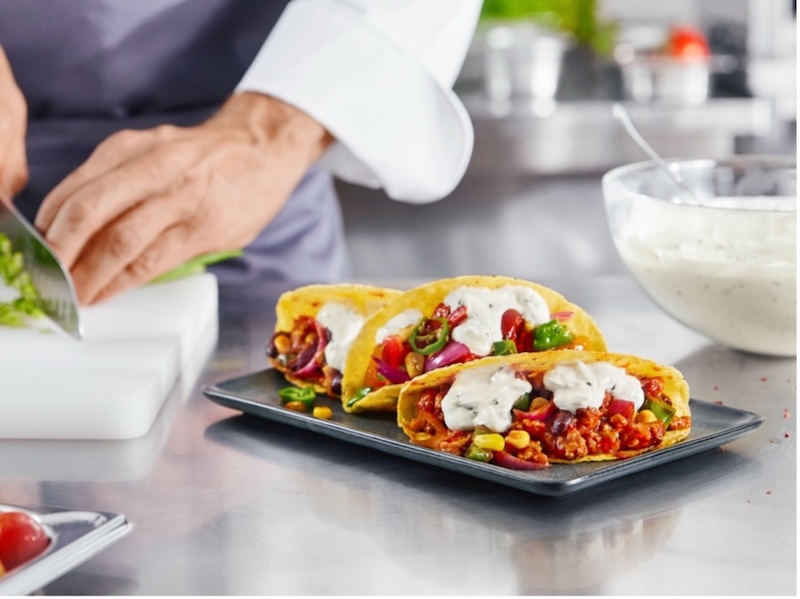 Ein rechteckiger Teller mit drei Nachos, gefüllt mit Chili und getoppt MILRAM Sour Cream
