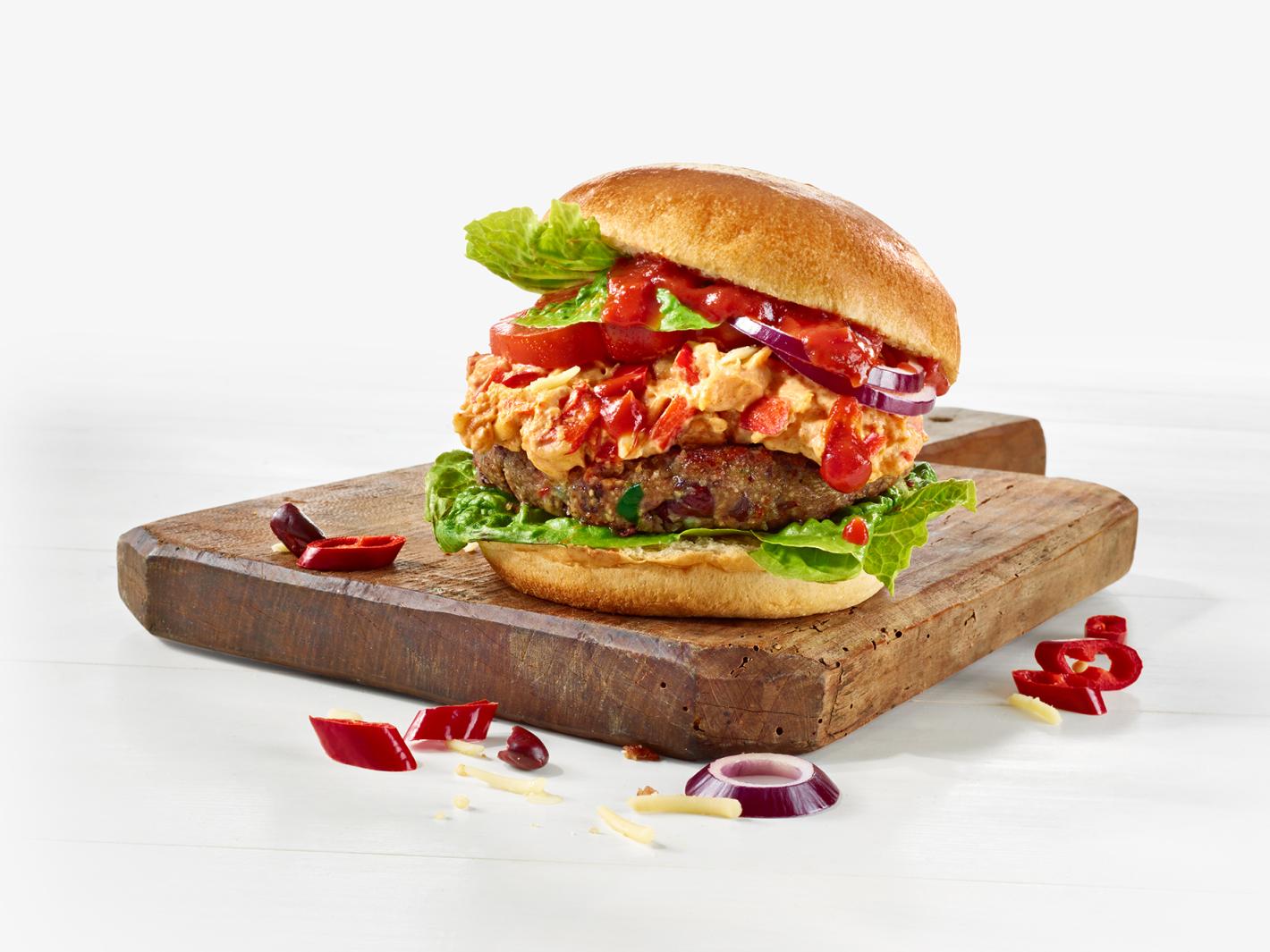 Burger auf einem Holzbrett belegt mit Salatblättern, pflanzlichem Patty, veganer Käse-Creme, Tomaten und Zwiebeln